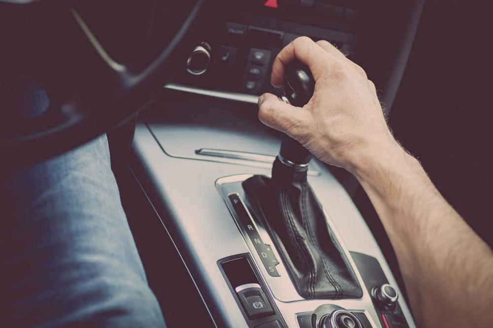 A person with their hand on the stick shift puts a car into gear